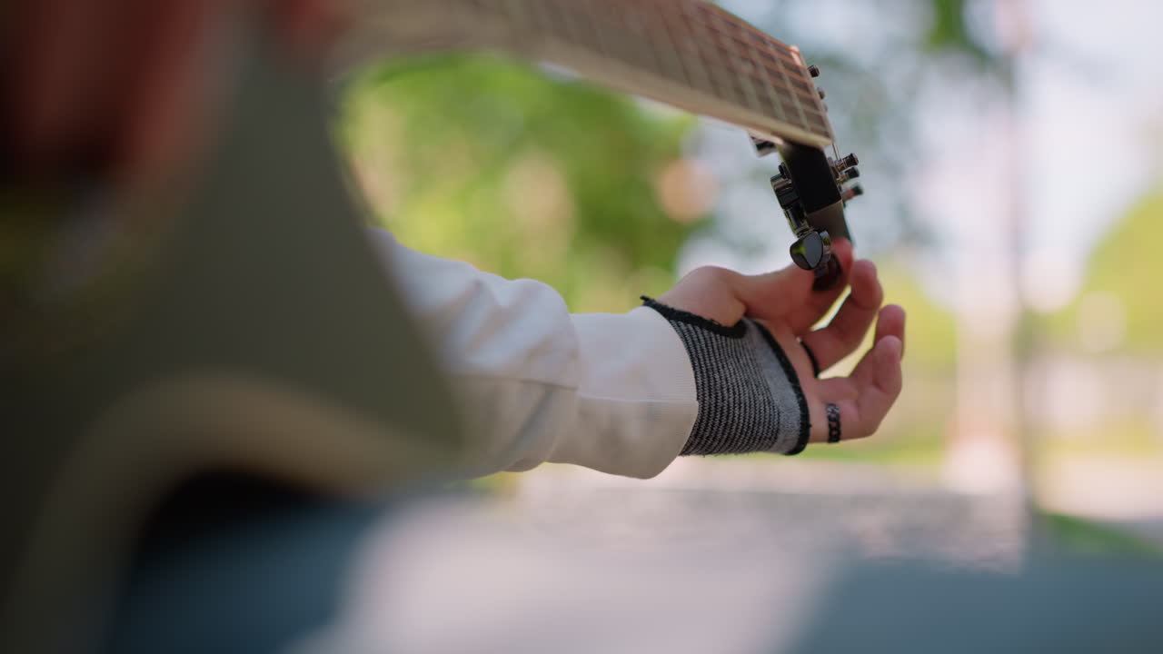 Güneş ışığı alan parkta bankta oturan birinin gitar akortlaması. Sakin bir park ortamında, gün ışığında gitarı kalibre etme. Parlak güneş ışığı altında, huzurlu bir park ortamının yanında birinin gitar tellerini ayarlaması