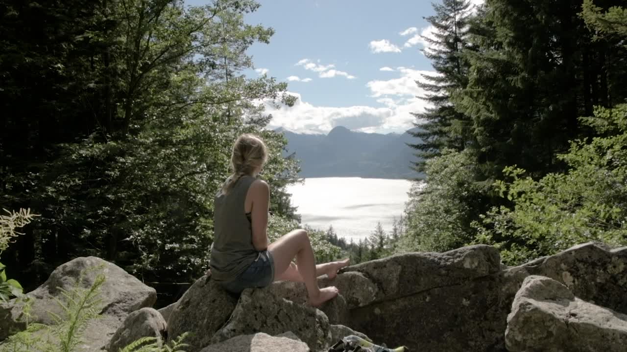 호수의 아름다운 전망을 즐기는 숲에 앉아있는 소녀