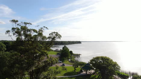 Volando-Sobre-Un-Parque-Junto-Al-Lago-Con-Un-Mirador-Mientras-Los-Caminantes-Caminan-Por-La-Hierba-En-Una-Hermosa-Tarde-De-Primavera-En-Florida