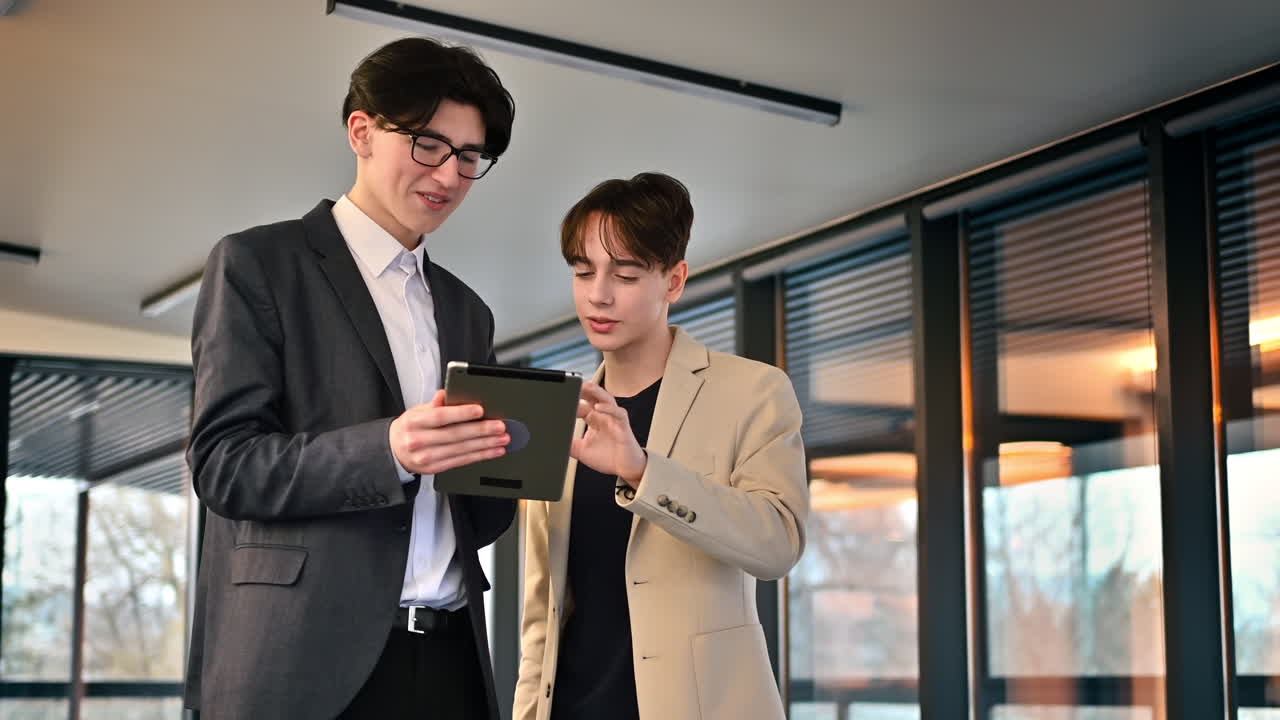 オフィスでタブレットを使ってビジネスについて話し合う若い従業員2人。スローモーション。
