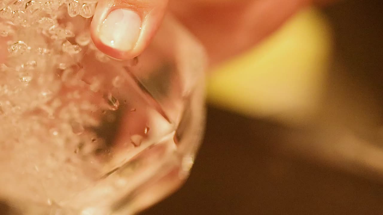 A detailed view of a hand rinsing a glass, highlighting bubbles and reflections.