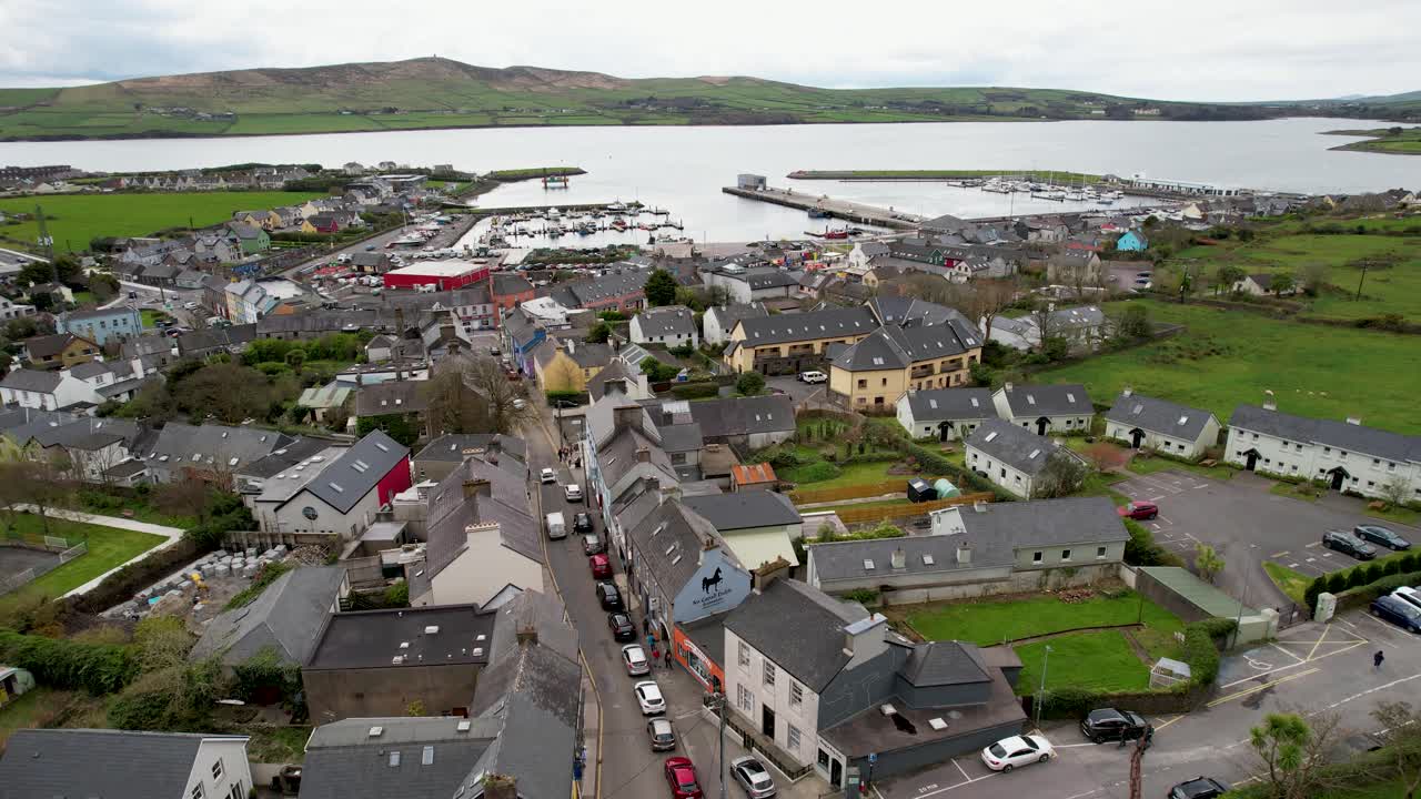 극적인 드론은 아일랜드의 딩글에 있는 교회를 지나가며 반도에서 구름이 가득한 날 항구에 있는 배로 날아갑니다.