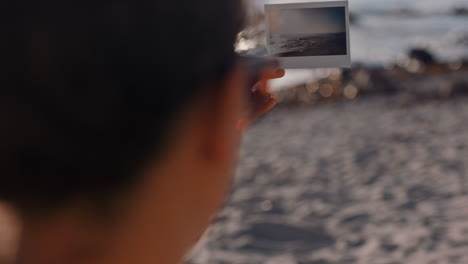 close-up-woman-holding-photograph-of-beautiful-seaside-ocean-at-sunset