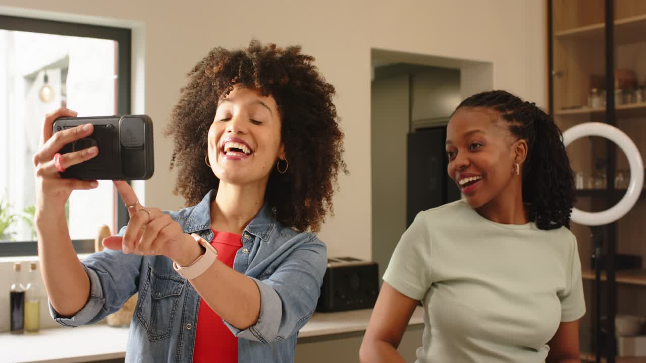 Diverse female friends positioning phone filming slicing avocado and pepper making salad in kitchen