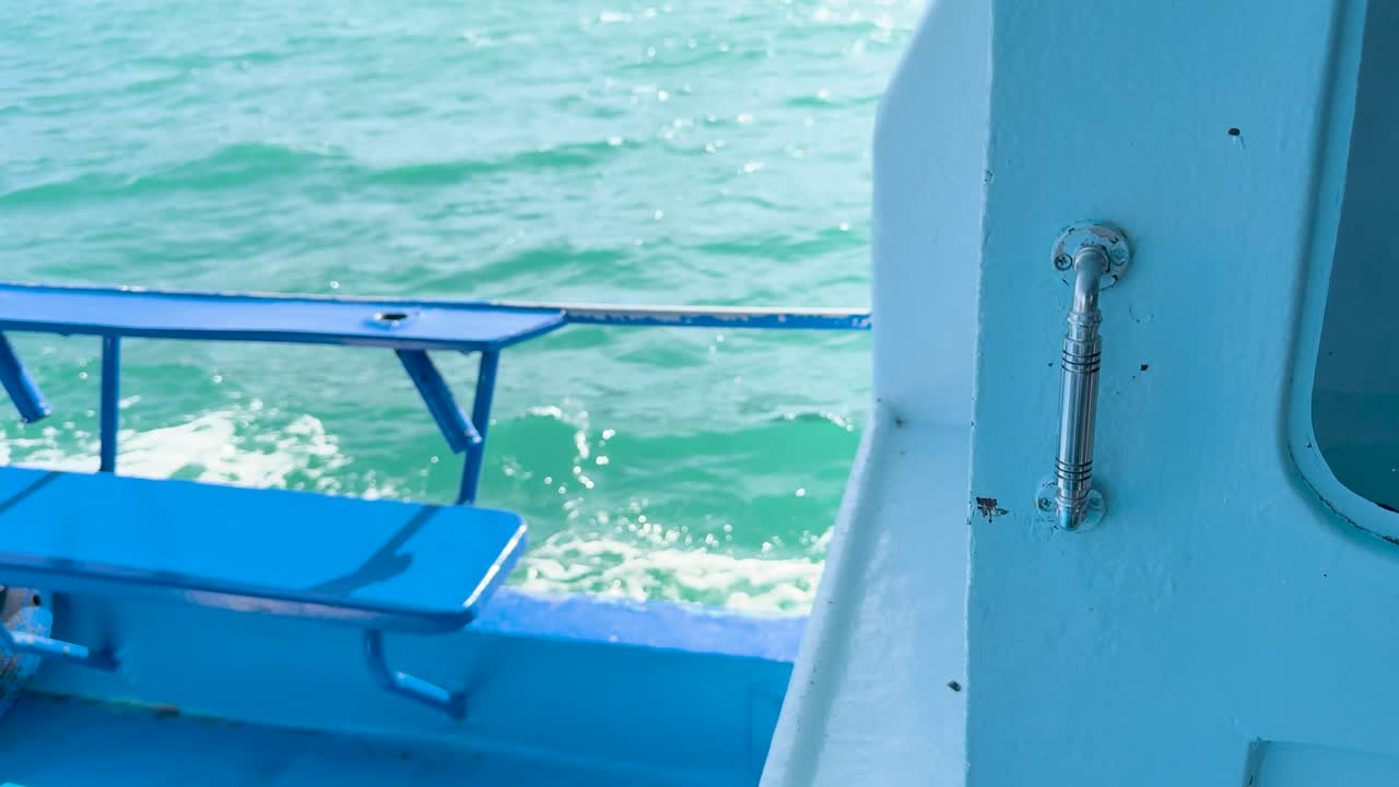 A boat glides through vibrant turquoise waters near Phuket, Thailand, with a focus on the metal handle and ocean waves