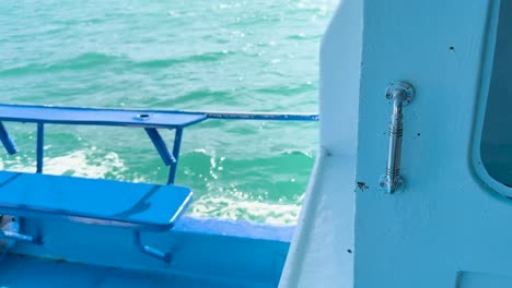 a boat glides through vibrant turquoise waters near phuket, thailand, with a focus on the metal handle and ocean waves
