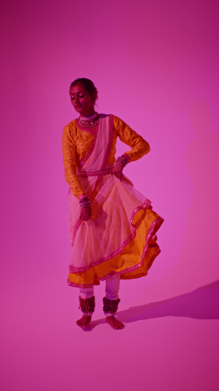 video vertical de larga duración en estudio de una bailarina de kathak que realiza un baile vestida con el vestido tradicional indio contra un fondo púrpura 1