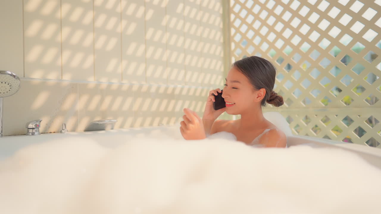 Pretty Asian Woman Calling on Smartphone in Foamy Bathtub