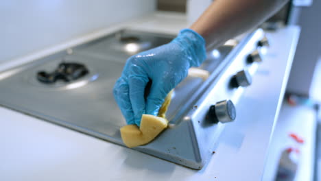 cleaning a kitchen stove with care. a person wearing gloves cleans a stainless steel stove top with a sponge, ensuring a tidy kitchen surface