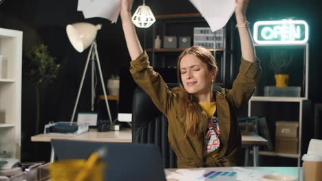 Portrait-of-happy-young-woman-throwing-papers-in-night-office-in-slow-motion