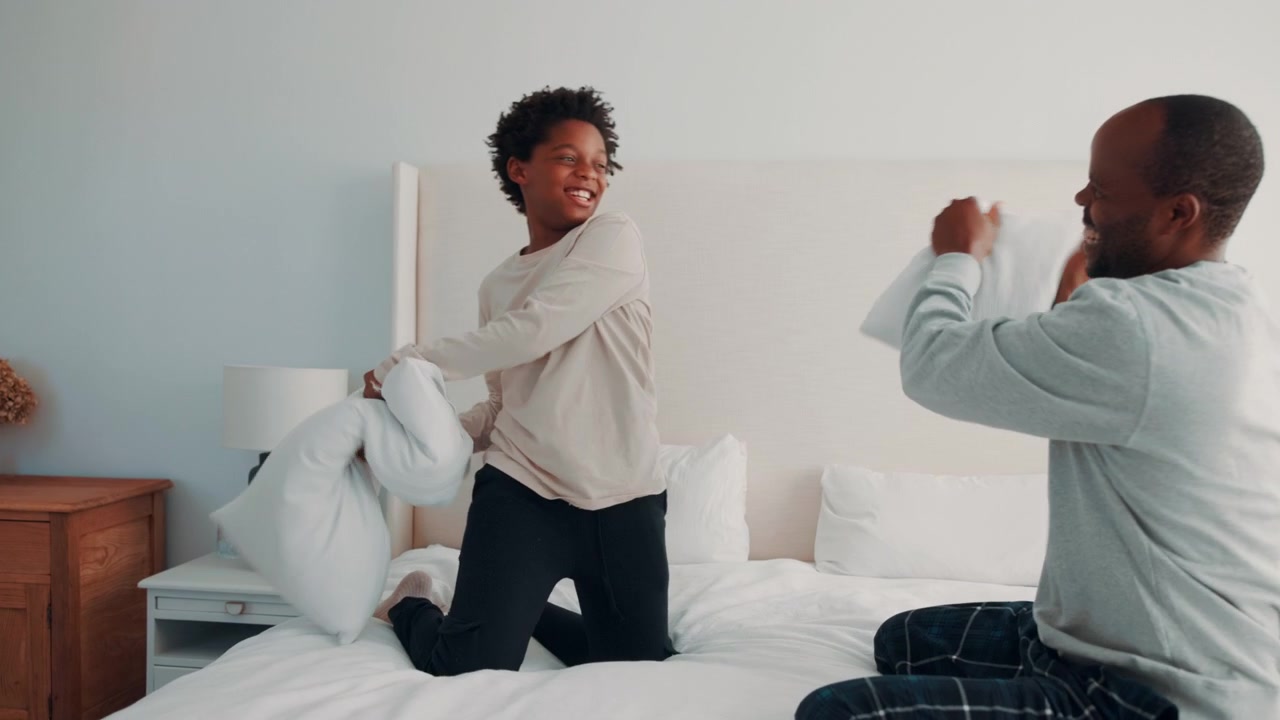 Father and Son Having a Playful Pillow Fight on Bed