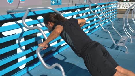 man with dark hair does ten push ups on bars at outdoor fitness course, medium shot