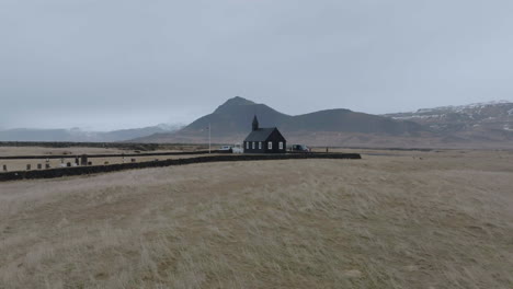 drone shot of church in búðir, iceland, black building in humid landscape on cloudy day