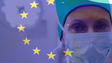 Animation-of-flag-of-europe,-close-up-of-caucasian-female-doctor-with-mask-standing-in-hospital