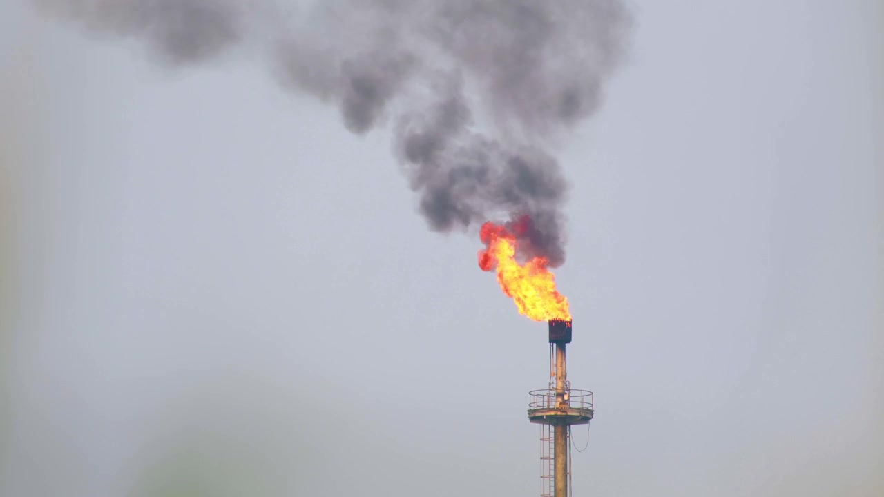 Torchère de raffinerie de pétrole avec un feu ardent rejetant une épaisse fumée noire dans le ciel bleu depuis la cheminée - images 4K.