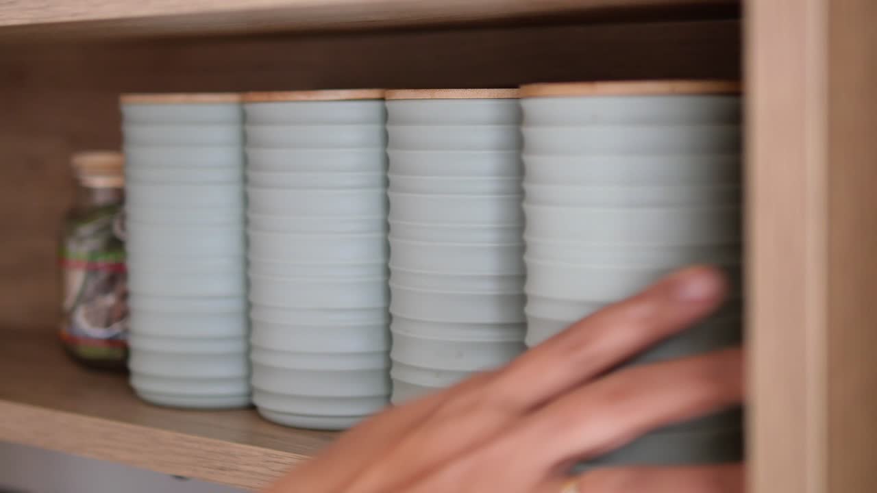 Mano che organizza contenitori portaoggetti azzurri su uno scaffale di legno