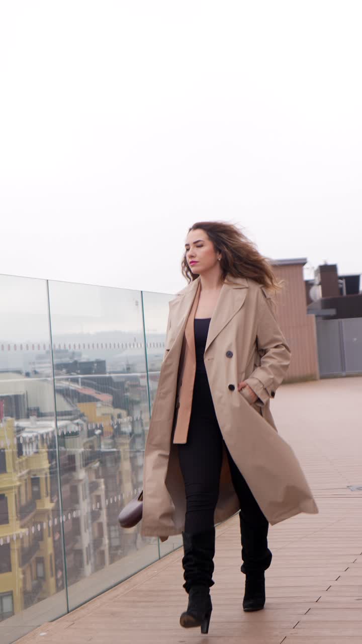 Donna elegante in trench che cammina su una terrazza urbana