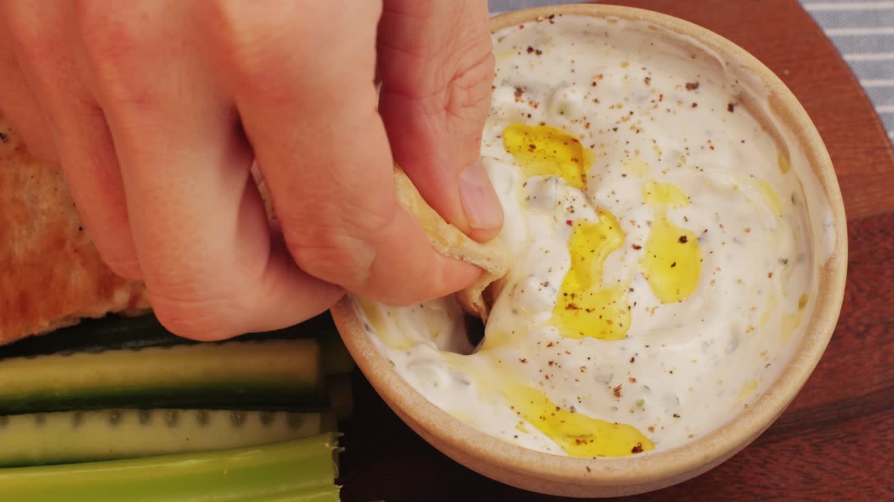 Hand Dipping Pita Bread in Tzatziki Sauce with Cucumber and Celery