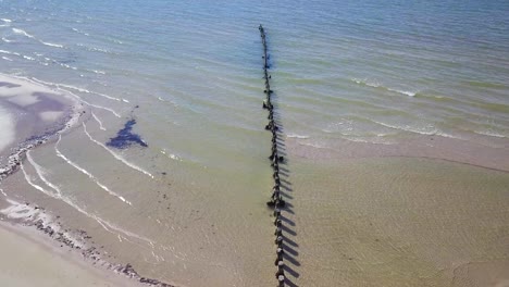 aerial birdseye view of baltic sea coast on a sunny day, old wooden pier, white sand coastline damaged by waves, coastal erosion, climate changes, wide angle drone shot moving forward