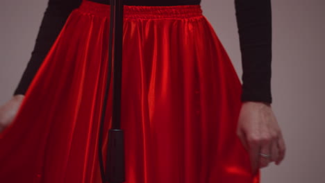 a faceless woman stands against a grey background, flicking her red skirt. the close-up shot captures the elegance and movement of the skirt