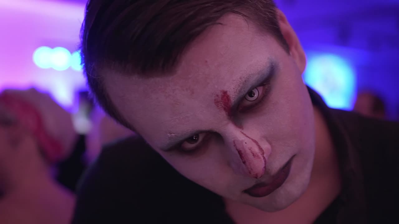 Face painted man closeup during carnival party in background, slowmo