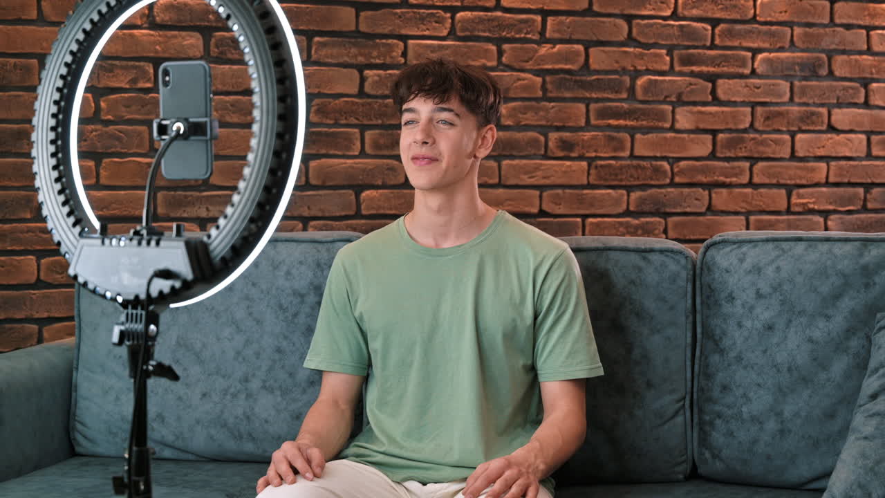 A young smiling man blogger influencer talking and shooting himself on smartphone on a tripod with ring light in a studio