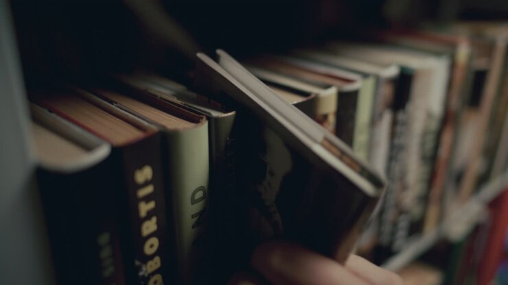 Mano di un uomo che sceglie e prende un libro da uno scaffale in una biblioteca pubblica