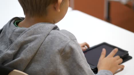 Vista-Trasera-Del-Niño-De-La-Escuela-Caucásica-Haciendo-Clic-En-La-Tableta-En-El-Aula,-De-Cerca