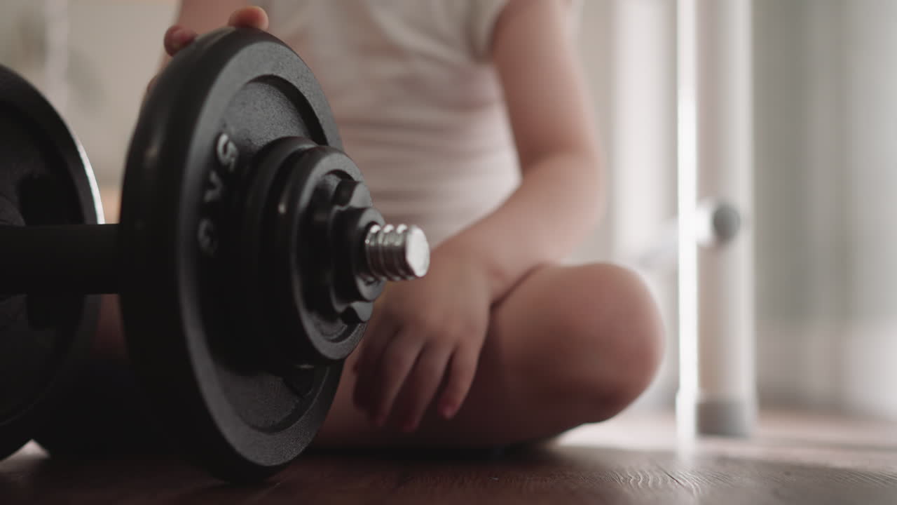 Little boy fixes gear detail near plate on heavy barbell