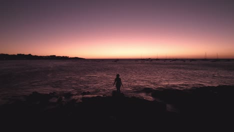 drone dolley shot over a woman standing at the stone and spreading her arms during a colorful sunset