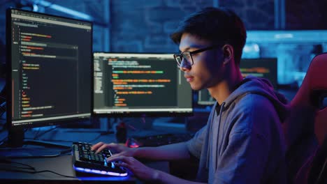 young programmer coding on multiple monitors in a dark, neon-lit room