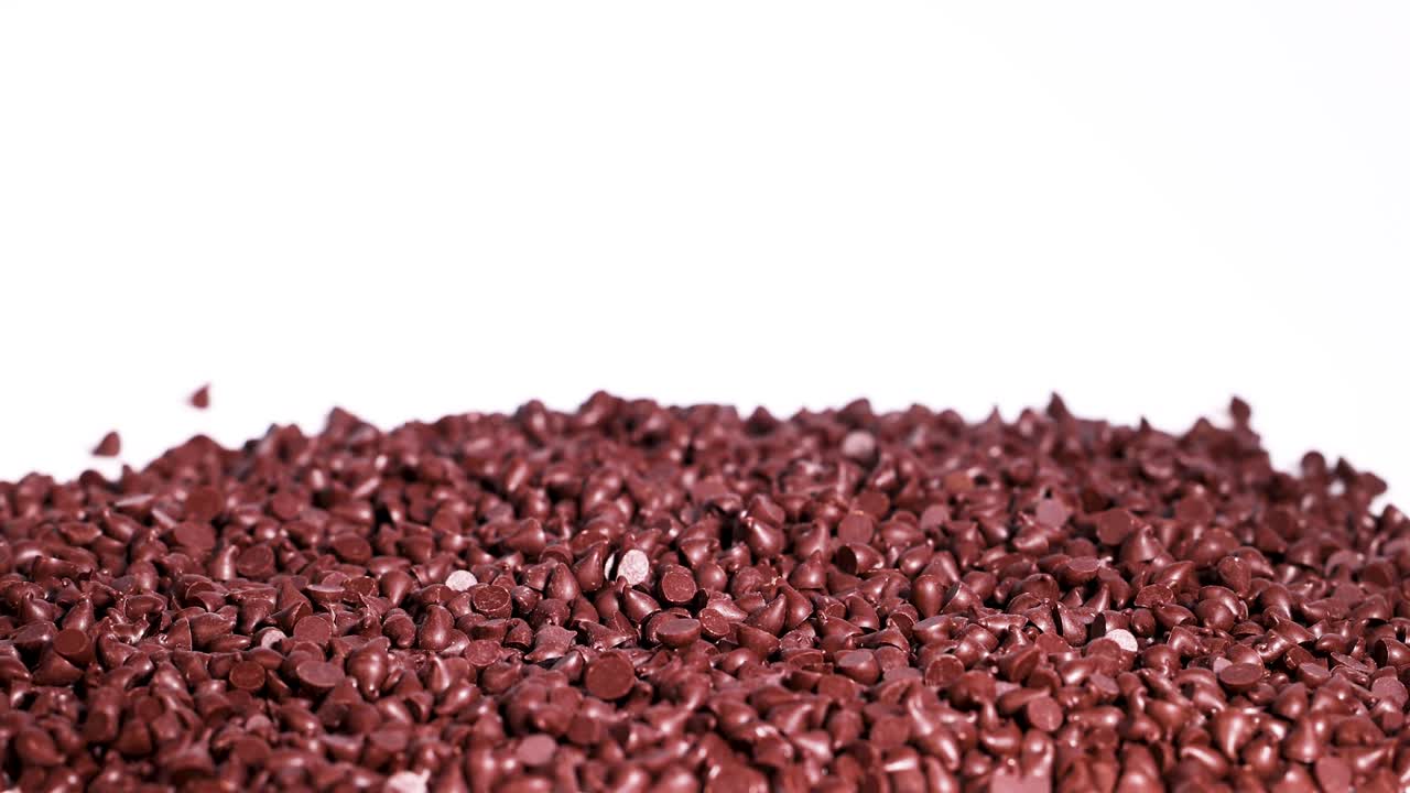 Chocolate drops cascade onto a pile against a white backdrop. High contrast lighting highlights texture and movement