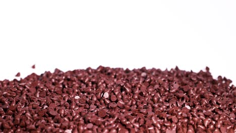 chocolate drops cascade onto a pile against a white backdrop. high contrast lighting highlights texture and movement