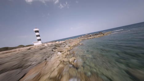 FPV-drone-forward-moving-shot-of-Punta-Plana-lighthouse-over-rocky-beaches-in-Faro-de-s'Estalella,-Mallorca,-Balearic-Islands,-Spain-on-a-sunny-day