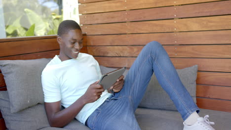 Relaxing on couch, african american man smiling and using tablet for entertainment