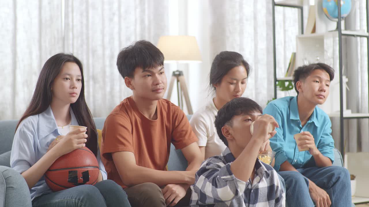 아시아 십대 들 은 집 에서 tv 에서 농구 경기 를 보는 동안 환호 하고, 먹고 마시고 있다