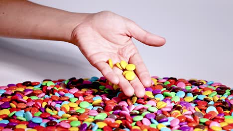 hand picks yellow candies from colorful pile