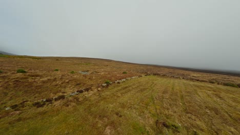 FPV-Drohne-Fliegt-Einen-Leeren-Hügel-Hinauf,-Der-Von-Grasfeldern-Bedeckt-Ist