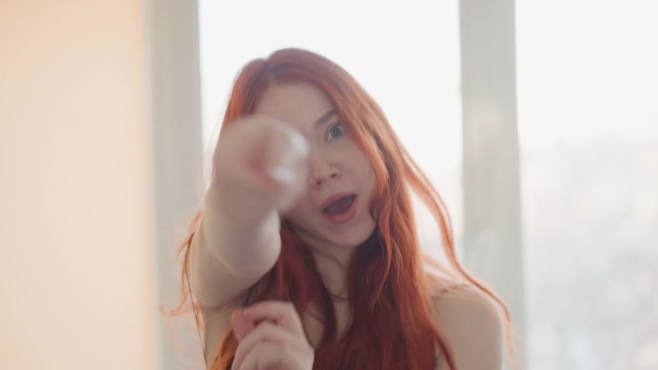 Mulher expressiva apreciando música. Mulher com cabelo ruivo flamejante dançando apaixonadamente. Mulher ruiva fazendo headbanging apaixonadamente perto de um vidro iluminado pelo sol com movimento energético e emoção expressiva