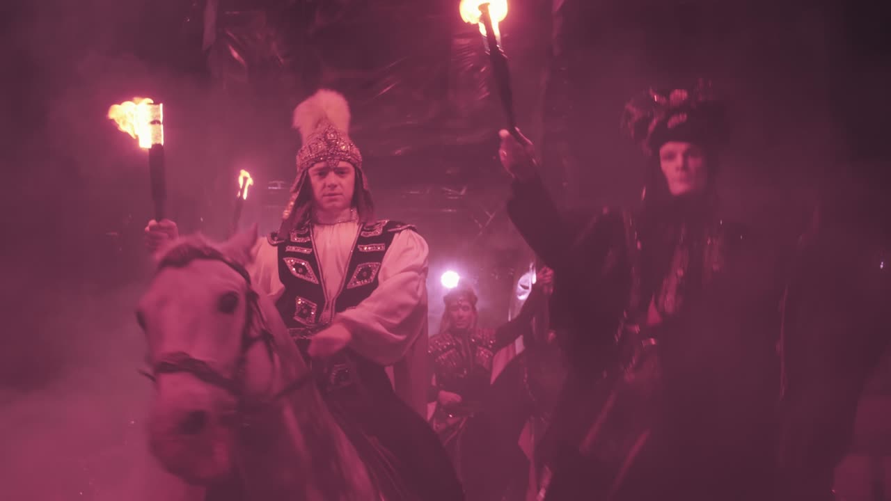 los jinetes salen de la niebla a la arena del circo, con antorchas en las manos, abrigos de lluvia revoloteando, actuación