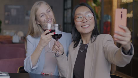two women taking a selfie while drinking wine at a restaurant