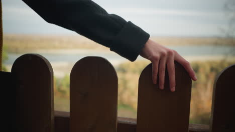 gentle touch of a woman's hand on a wooden fence, with blurred trees and a river in the autumn background, evoking tranquility and connection with nature