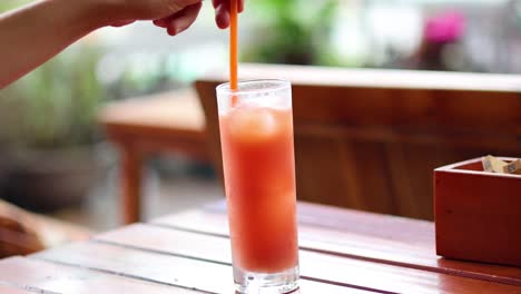 hand stirring a glass of iced drink with straw