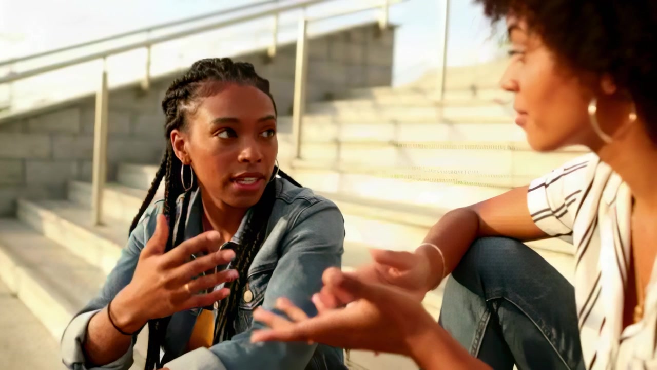 Smiling left woman in denim jacket catching up with woman in striped top on steps, gesturing