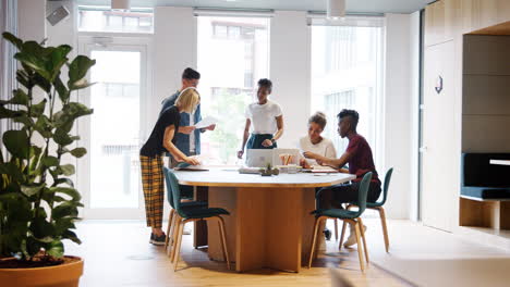 Creative-millennial-team-doing-paperwork-together-standing-and-sitting-around-a-table-in-a-large-office,-full-length-view