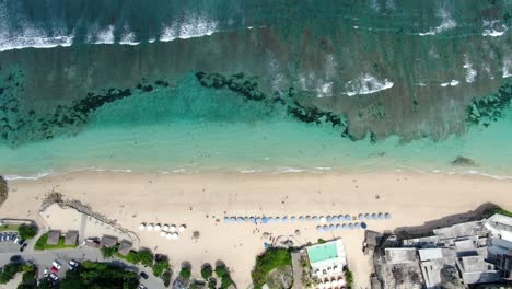 Imágenes-De-Drones-De-La-Playa-Melasti-En-Uluwatu-Bali,-Donde-Se-Podían-Ver-Numerosas-Sombrillas,-Hoteles-Y-Olas-Que-Se-Dirigían-Hacia-La-Playa