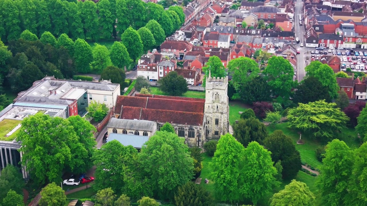 Images aériennes par drone du Centre des Arts de Salisbury dans le Wiltshire, montrant l'ancien bâtiment d'église historique, les arbres environnants, le parc verdoyant, les rues résidentielles avoisinantes et les toits du centre-ville.