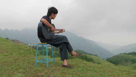 Side-view-of-musician-playing-a-guitar-on-the-top-of-a-mountain