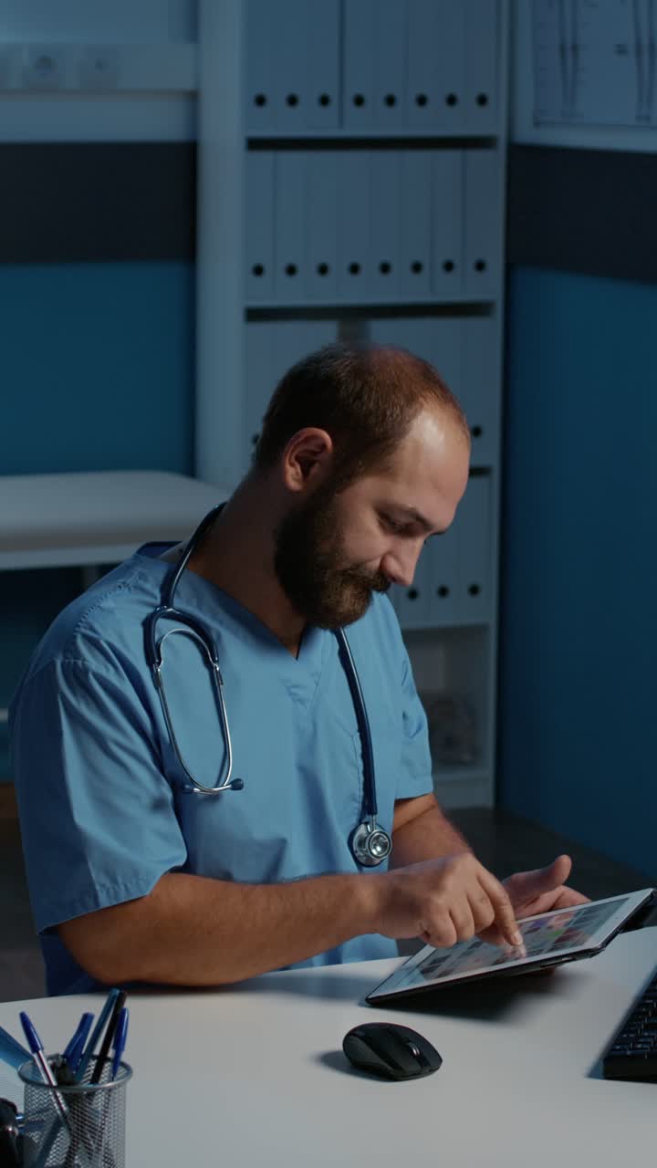 Vertical video: Physician nurse sitting at desk holding tablet computer analyzing patient illness report