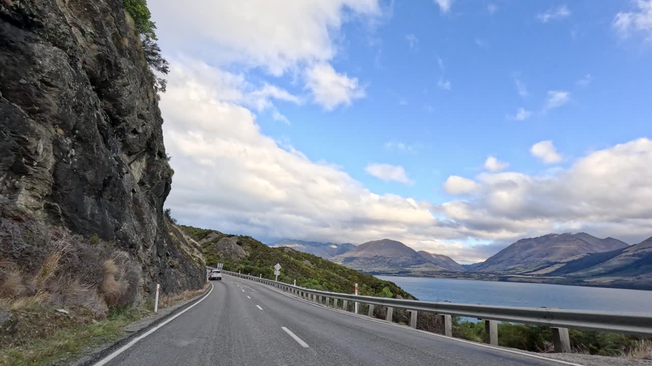 Vehicle travels winding mountain road with lake and mountains, daylight, wide angle, smooth camera movement